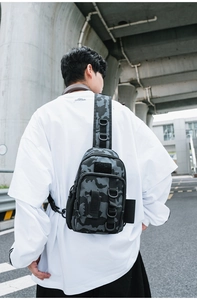 Outdoor street view of a tactical grey camo crossbody bag with D-ring and velcro detail
