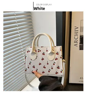 Detail showing white cherry print crossbody bag with handles and matching slim strap