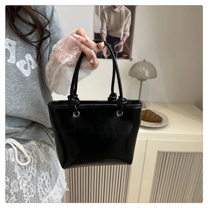 Detail view of glossy black bucket bag with knotted handles and metallic ring hardware