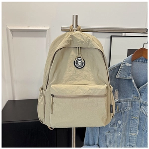 Close-up of beige nylon backpack featuring a front zipper pocket and round brand logo patch