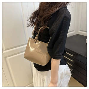Detail of khaki patent leather bucket bag featuring decorative knotted handles and metal buckle