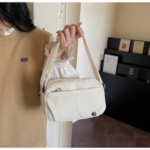 Détail d'un sac bandoulière en toile beige à poches multiples avec logo métallique