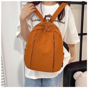 Detail of orange minimalist backpack showing dual vertical zippers and side brand label