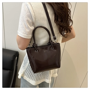 Detail view of dark brown patent leather bucket bag with knotted handle and silver buckles
