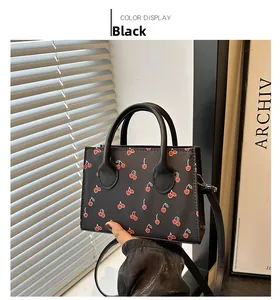 Close-up of black mini tote bag featuring red cherry prints and removable shoulder strap