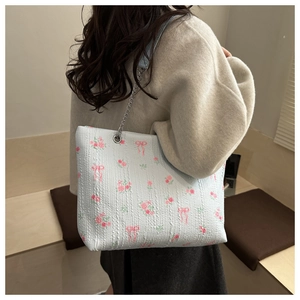 Detailed side view of light blue floral tote bag with chain strap worn by a model