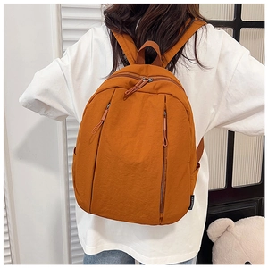Detail view of ginger yellow nylon backpack featuring vertical zip pockets and side brand label