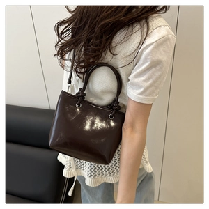 Close-up of dark brown glossy leather bucket bag with decorative handle knots and silver rings