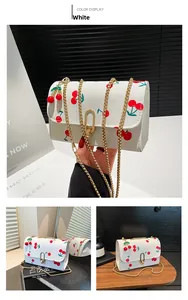 Detail of white cherry print crossbody bag with gold chain and cherry shaped pendant charm