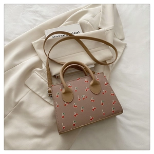 Close-up of pink-brown square crossbody bag featuring vibrant red cherry prints and metal hardware