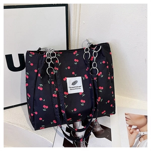 Detail of cherry print tote bag featuring metallic chain strap and black canvas material