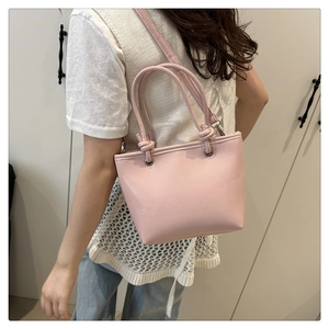 Pale pink minimalist tote bag with knotted handles and detachable strap on person