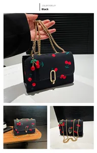 Detail of black canvas crossbody bag with red cherry print and golden chain strap