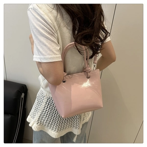 Side view of pink patent leather bucket bag worn by model with silver metal details