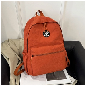 Close-up of burnt orange nylon backpack with circular logo and durable zipper pockets