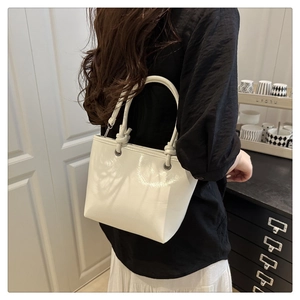 Detail of white glossy patent leather bucket bag with a unique knotted top handle design