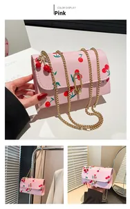 Detail view of pink crossbody bag with cherry prints and golden chain shoulder strap