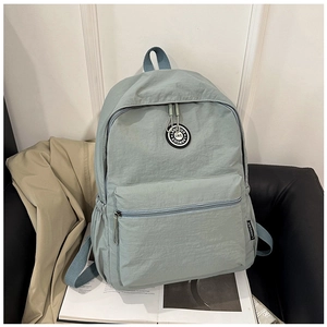 Detail view of light blue nylon backpack showing the front zip pocket and brand logo patch