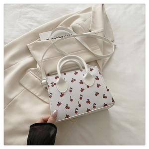 Top-down view of cream-white cherry print crossbody bag on a beige blazer background