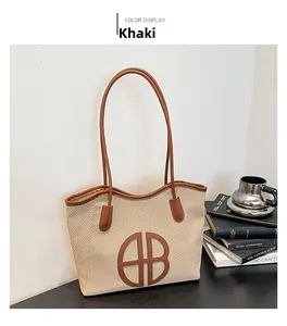 Detail of khaki woven tote bag with brown leather handles and circular AB logo patch