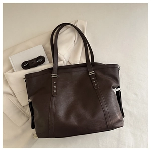 Detailansicht braune Totebag mit Sternen-Nieten auf elegantem weißem Anzug-Hintergrund
