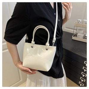 Detail showing white glossy mini bucket bag with knot handle and metal eyelets on shoulder strap