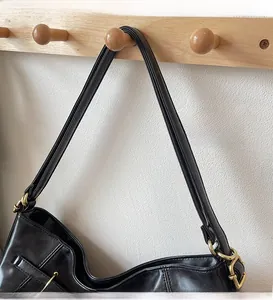 Close-up of black leather shoulder strap with golden metal rings on a wooden hook