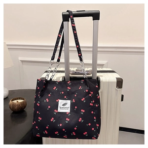 Detail of cherry print shoulder bag with metal chain strap hanging on luggage handle