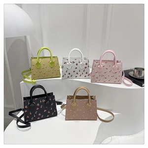 Five small cherry print tote bags in diverse colors displayed on a modern white stand