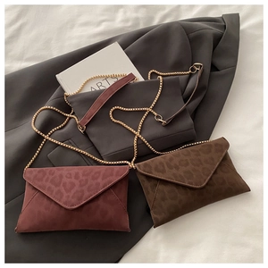 Close-up of leopard print envelope bags with golden ball chains on a grey blazer