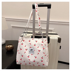 Detail of cherry print tote bag featuring a white strap with silver chain and fabric patch