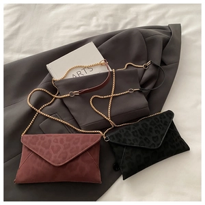 Detail of trendy leopard-print envelope crossbody bags with gold chain straps in black and red
