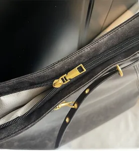 Detail of a smooth golden zipper on a black leather tote bag with stylish herringbone lining