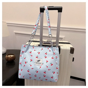 Close-up of light blue cherry print tote bag with metal chain strap on a suitcase