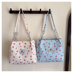 Detail of canvas tote bags with cherry prints, metal chain straps, and woven labels