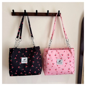 Detail of pink and black cherry print tote bags hanging on a minimalist wall hook