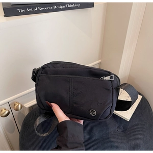 Détail d'un sac bandoulière en nylon noir minimaliste avec fermeture éclair et logo rond