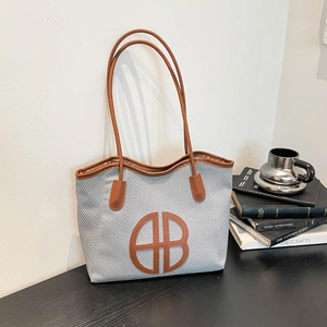 Chic commuter tote bag with brown leather handles and letter logo on grey textured canvas