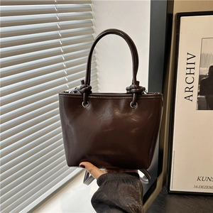 Minimalist deep brown glossy leather tote bag with unique knotted handles and silver eyelets