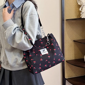 Black cherry print tote bag with metal chain strap shown on a model in a minimal room