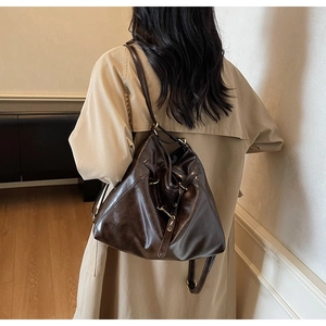 Brown leather tote bag shown on a model wearing a beige trench coat in a cozy room