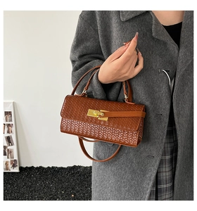 Detail view of brown woven texture small square bag with golden metal lock and strap