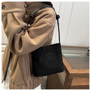 Détail du sac à main en daim noir avec texte embossé et bandoulière à nœuds sophistiquée