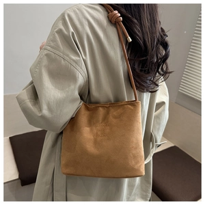 Détail du sac seau en daim marron avec gravure classique et bandoulière à nœud décoratif
