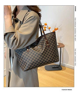 Detail view of large tote bag featuring brown M-letter print and golden bow detail