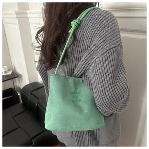 Détail du sac seau en daim vert clair avec broderie et poignée à cordon noué élégant