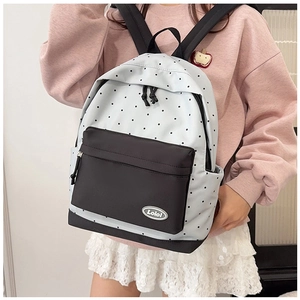 Detailed close-up of a cream polka dot backpack with a black zipper pocket and brand logo