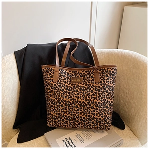 Detail of leopard print tote bag featuring a gold FASHION plaque and brown leather handles