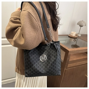 Detail of black tote bag with M-pattern print and leather-chain shoulder strap on model