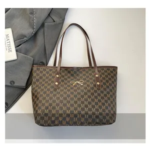 Close-up of brown tote bag with M-letter pattern, golden bow, and metallic ring hardware